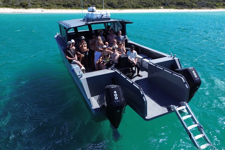 Group of people on a motorboat in clear blue water near a sandy shore.