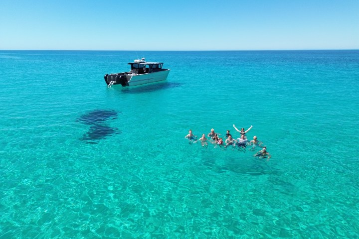 Boat and group of people swimming in clear blue ocean under a sunny sky.