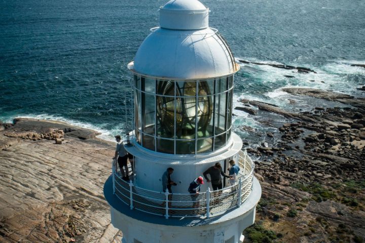 Aerial view of a lighthouse with people on its balcony by the ocean.