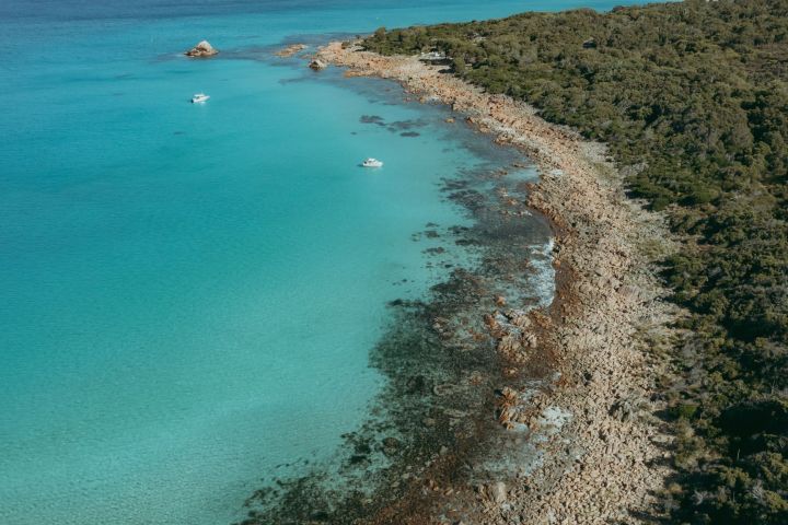 Aerial view of a rocky coastline with turquoise water and two boats near the shore.