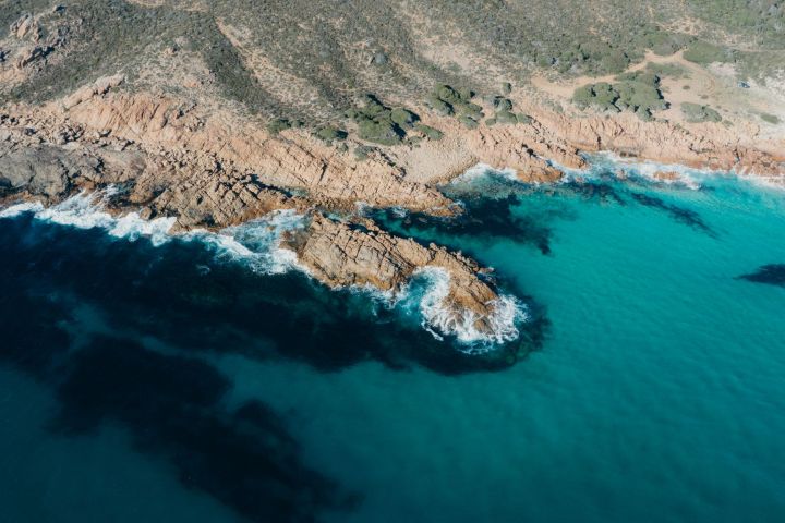 Aerial view of rocky coastline with turquoise water and waves crashing on the shore.