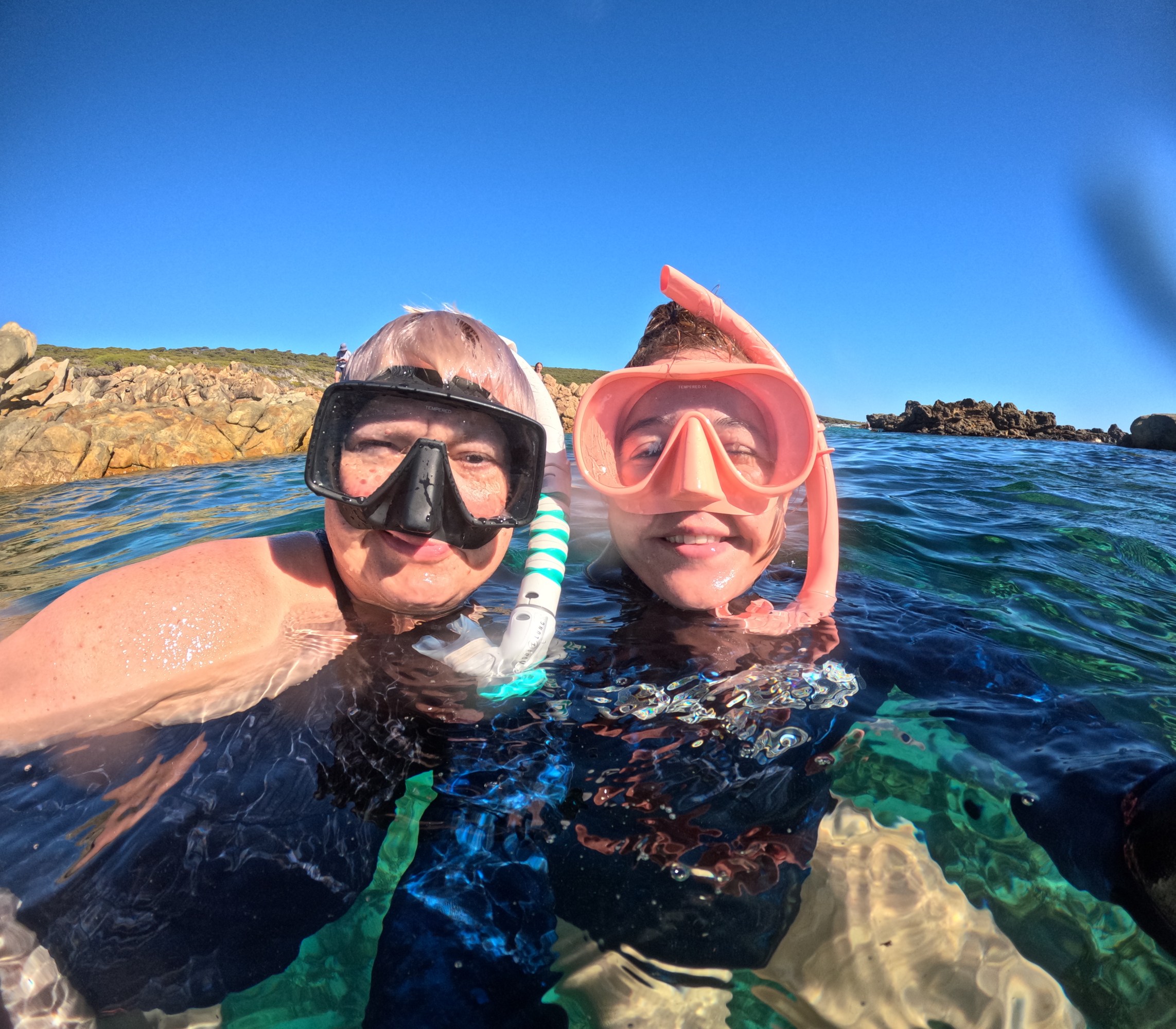 Two people snorkeling in clear water near rocky shoreline.