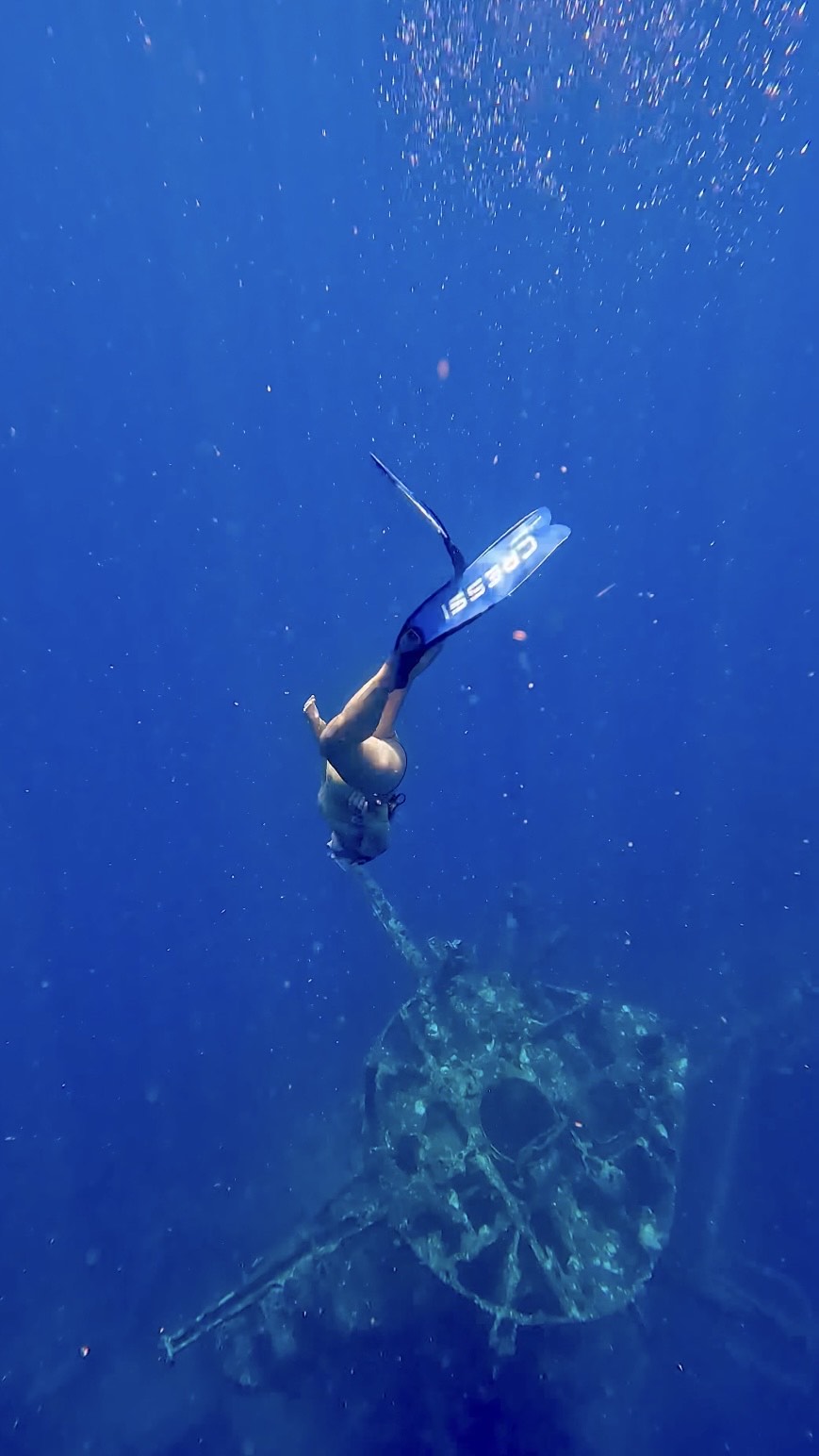 Diver with fins swims above underwater structure in deep blue sea.