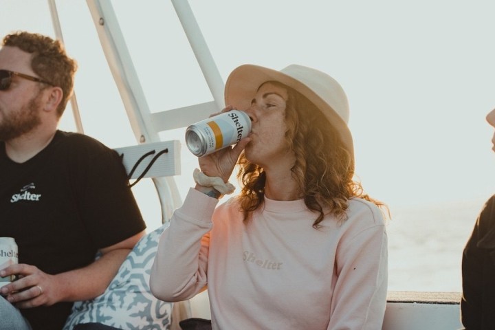 Two people on a boat, one drinking from a can, both wearing 'Shelter' shirts.