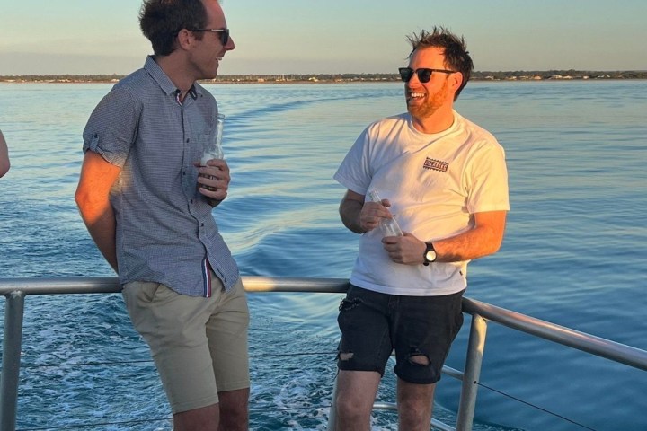 Two men laughing on a boat with a scenic ocean view at sunset.