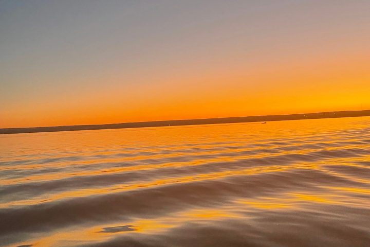 Calm ocean waves reflecting a vibrant orange sunset under a clear sky.
