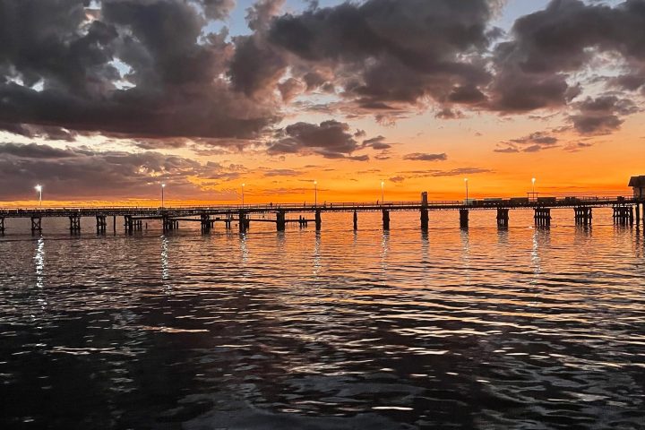 A pier over water at sunset with colorful sky and clouds.