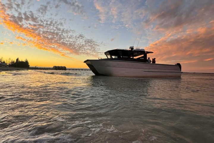 Boat on calm water with colorful sunset and cloudy sky in the background.