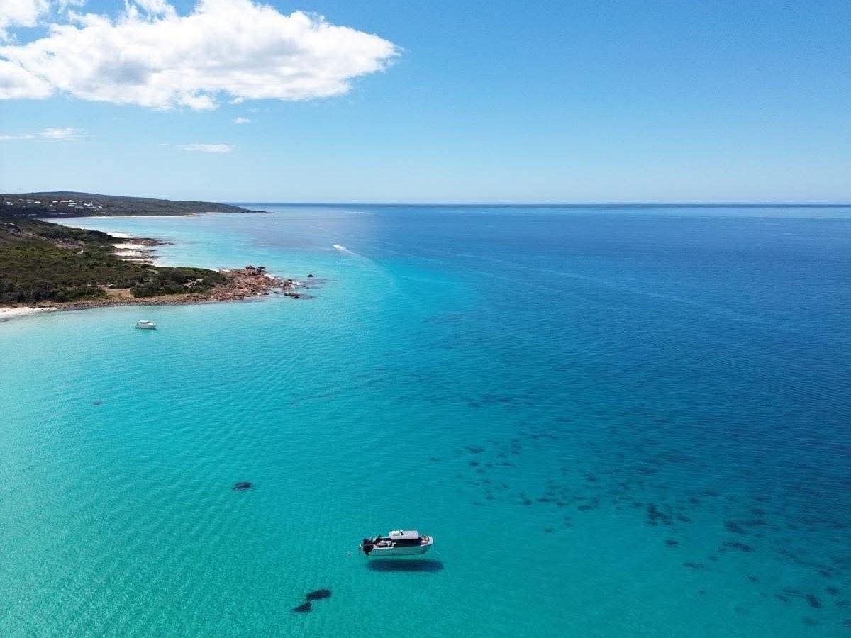 Aerial view of a boat on clear blue ocean near a coastline.