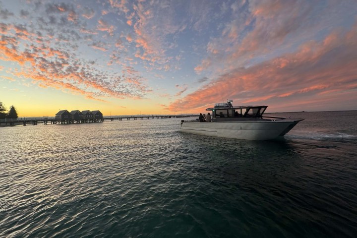 Boat on water at sunset with overwater buildings and colorful sky